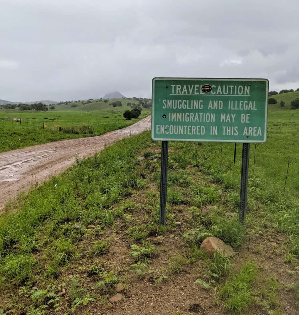 green sign along box canyon road in southern arizona that reads travel caution smuggling and illegal immigration may be encountered in this area